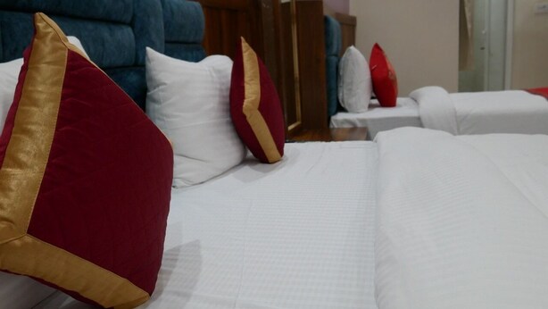 Quarto de hotel com uma cama grande, várias almofadas, cabeceira azul e mesa de cabeceira branca.