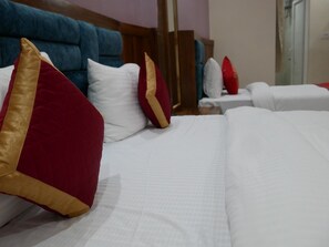 Una habitación de hotel con una cama grande, varios almohadones, un cabecero azul y una mesita de noche blanca.