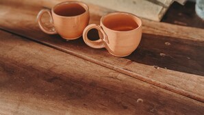 Deux gobelets en cuivre sur une surface en bois, avec une serviette à rayures, une petite plante et une bouteille en arrière-plan.