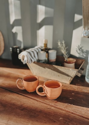 Deux gobelets en cuivre sur une surface en bois, avec une serviette à rayures, une petite plante et une bouteille en arrière-plan.