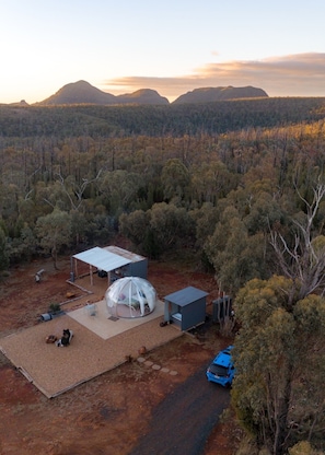 Une cabane isolée dotée d’une grande structure en forme de dôme transparent, d’un patio couvert et d’un petit abri de jardin.