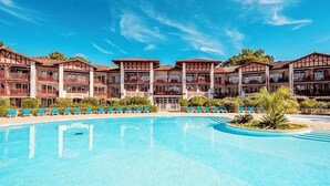 Un hotel con una piscina grande, varios balcones y un jardín tropical.