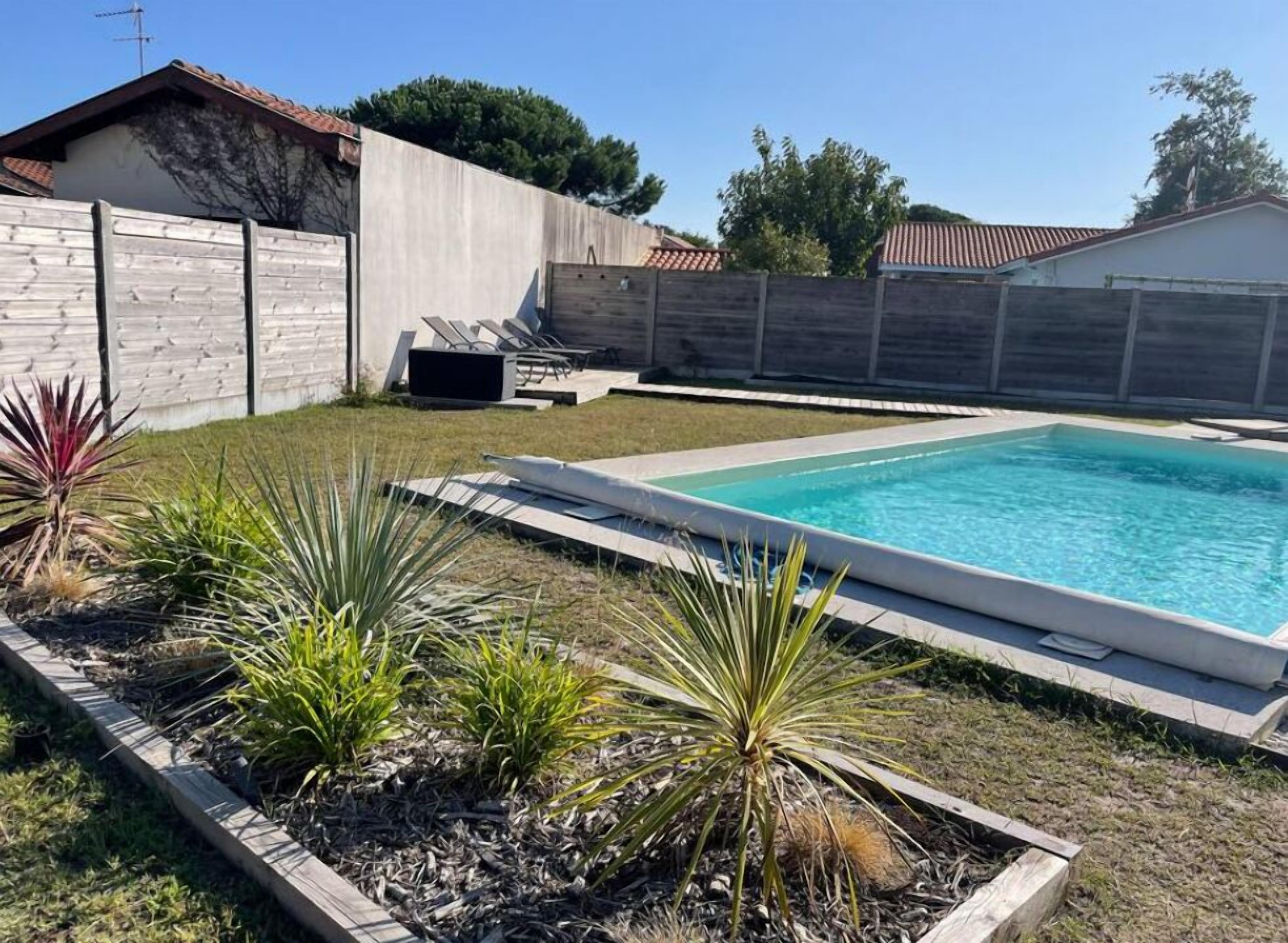 Piscina retangular com deck de concreto, rodeada por um muro de pedra baixo e diversas plantas.