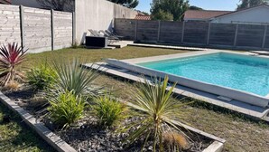 A rectangular swimming pool with a concrete deck, surrounded by a low stone wall and various plants.