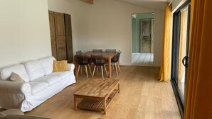 A living room with a white sofa, a wooden coffee table, and a dining table with chairs.