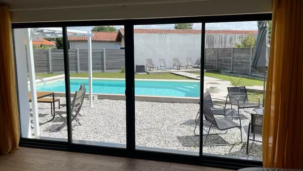 A room with a large sliding glass door leading to a backyard with a swimming pool, patio furniture, and a fenced area.