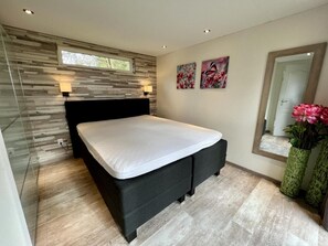 Un dormitorio moderno con cama, separador de vidrio, pared de madera, ventana y espejo.