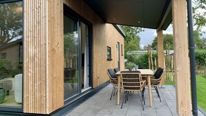 Eine moderne Terrassenanlage im Freien mit Holztisch und -stühlen, großen Schiebeglastüren und einer überdachten Sitzgruppe.