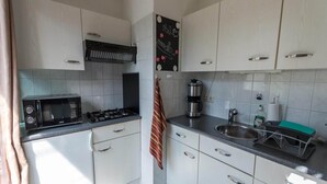 A compact kitchen with white cabinets, a microwave, a gas stove, a coffee maker, and a sink. - Bungalow in North Holland Coast (Sint Maartensvlotbrug)