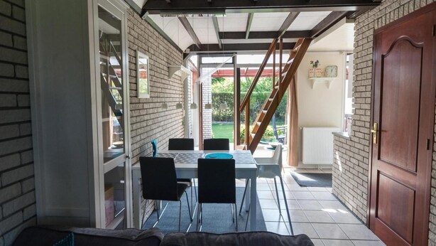 A covered patio with a table and chairs, a wooden staircase, and a brick wall. - Bungalow in North Holland Coast (Sint Maartensvlotbrug)