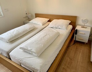 A double bed with white linens and two bedside tables, one with a fan and the other with a lamp. - Vacation Bungalow for 4 Persons (Sint Maartensvlotbrug)