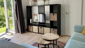 Un salon avec un téléviseur, un canapé, une table basse et une grande fenêtre avec des rideaux.