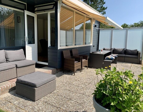 An outdoor patio with wicker furniture, a covered seating area, and a potted plant. - Spacious Bungalow Surrounded Large Garden (Sint Maartensvlotbrug)