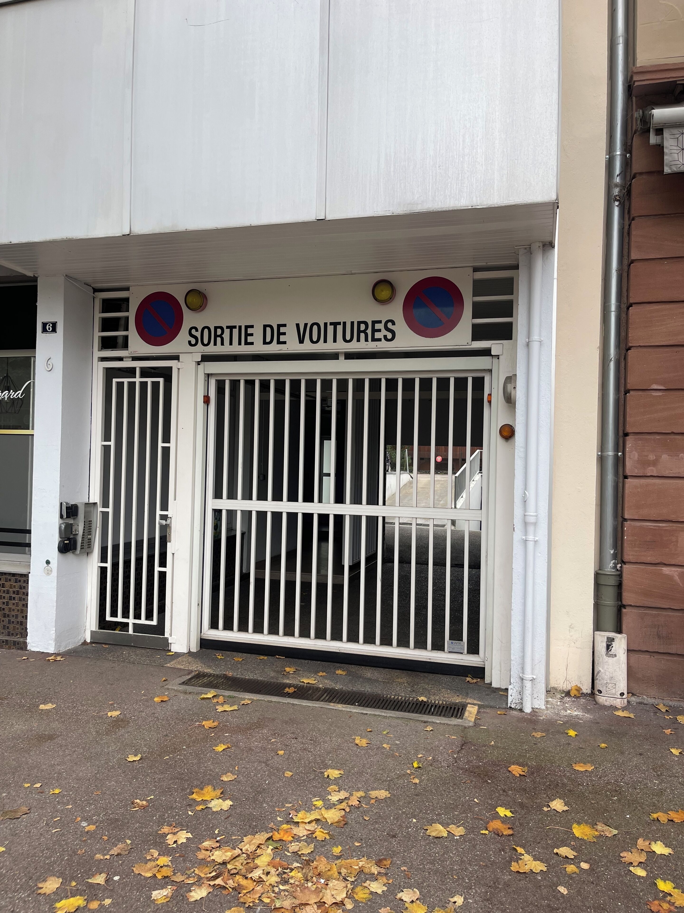 Une entrée fermée par une barrière, avec un panneau indiquant « SORTIE DES VÉHICULES » et un symbole interdisant le stationnement.