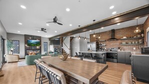 Cozinha moderna com ilha central, eletrodomésticos embutidos e área de jantar com mesa de madeira e banquetas.