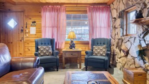 A cozy room with two leather sofas, a wooden coffee table, a stone wall, and a window with checkered curtains.