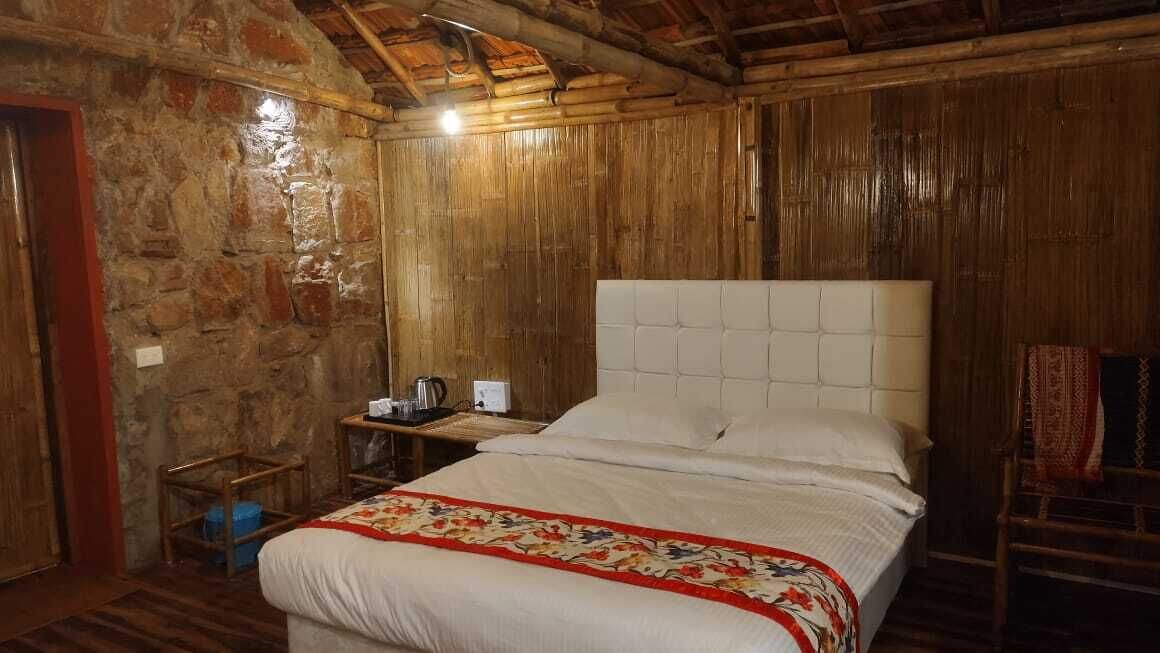 Una habitación de madera con una cama, una mesita con un hervidor y una silla.