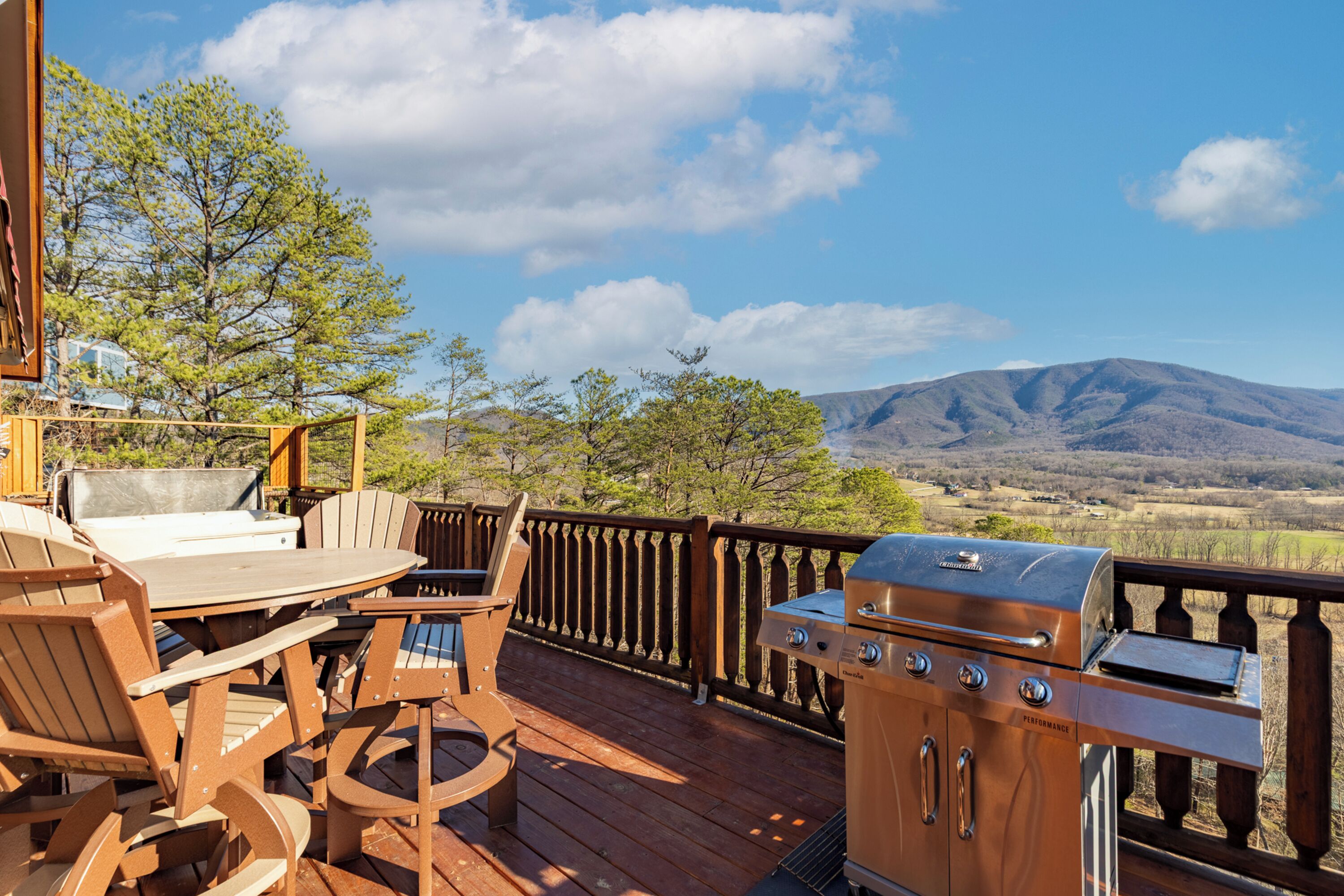 A wooden deck with outdoor furniture, a grill, and a scenic mountain view.