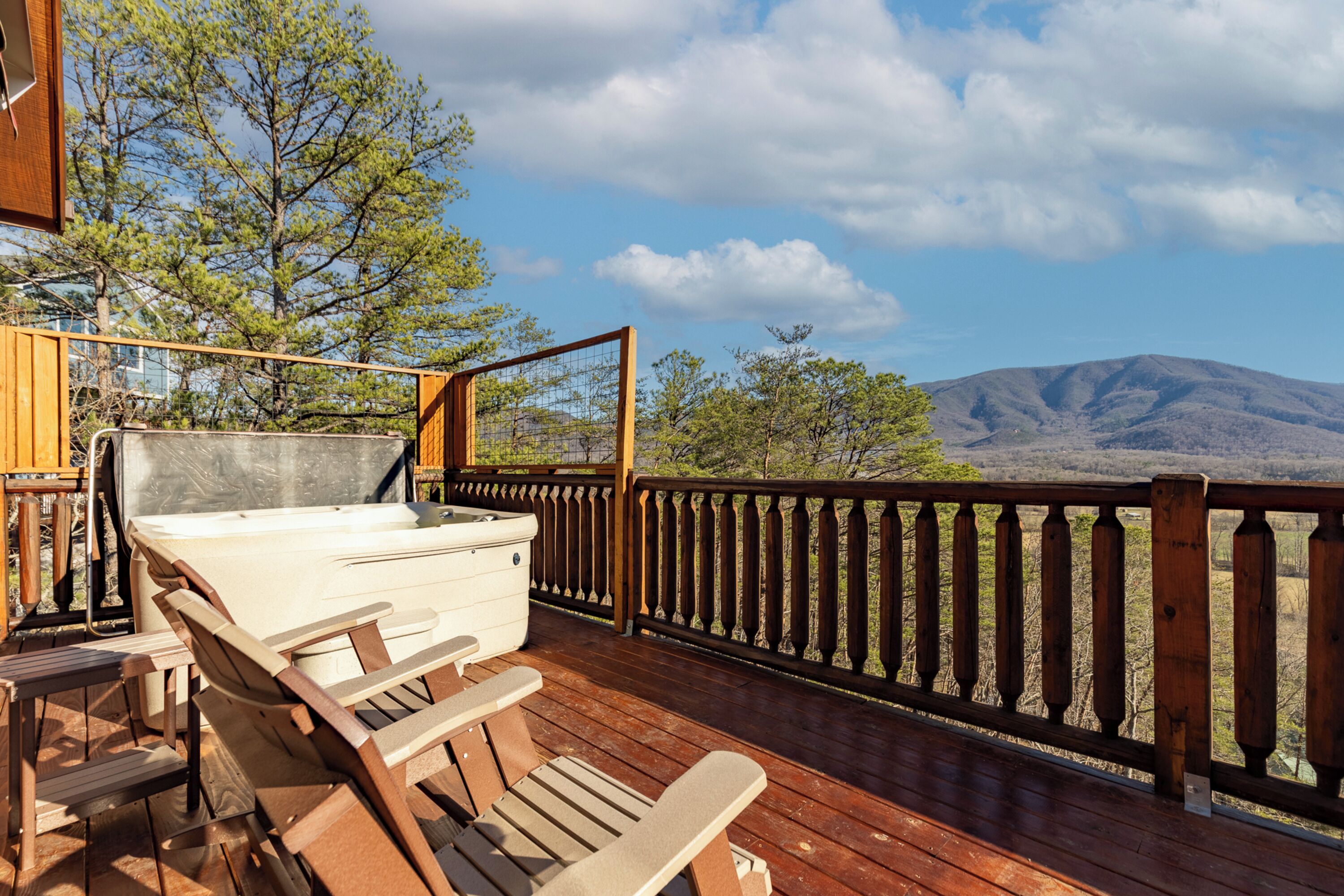 A wooden deck with a hot tub, wooden chairs, and a view of mountains.