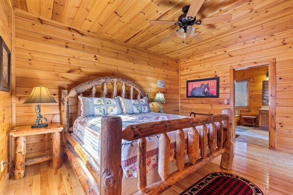 A wooden cabin bedroom with a bed, two bedside tables with lamps, a ceiling fan, and a framed picture on the wall. - Awesome Endeavor (Sevierville)