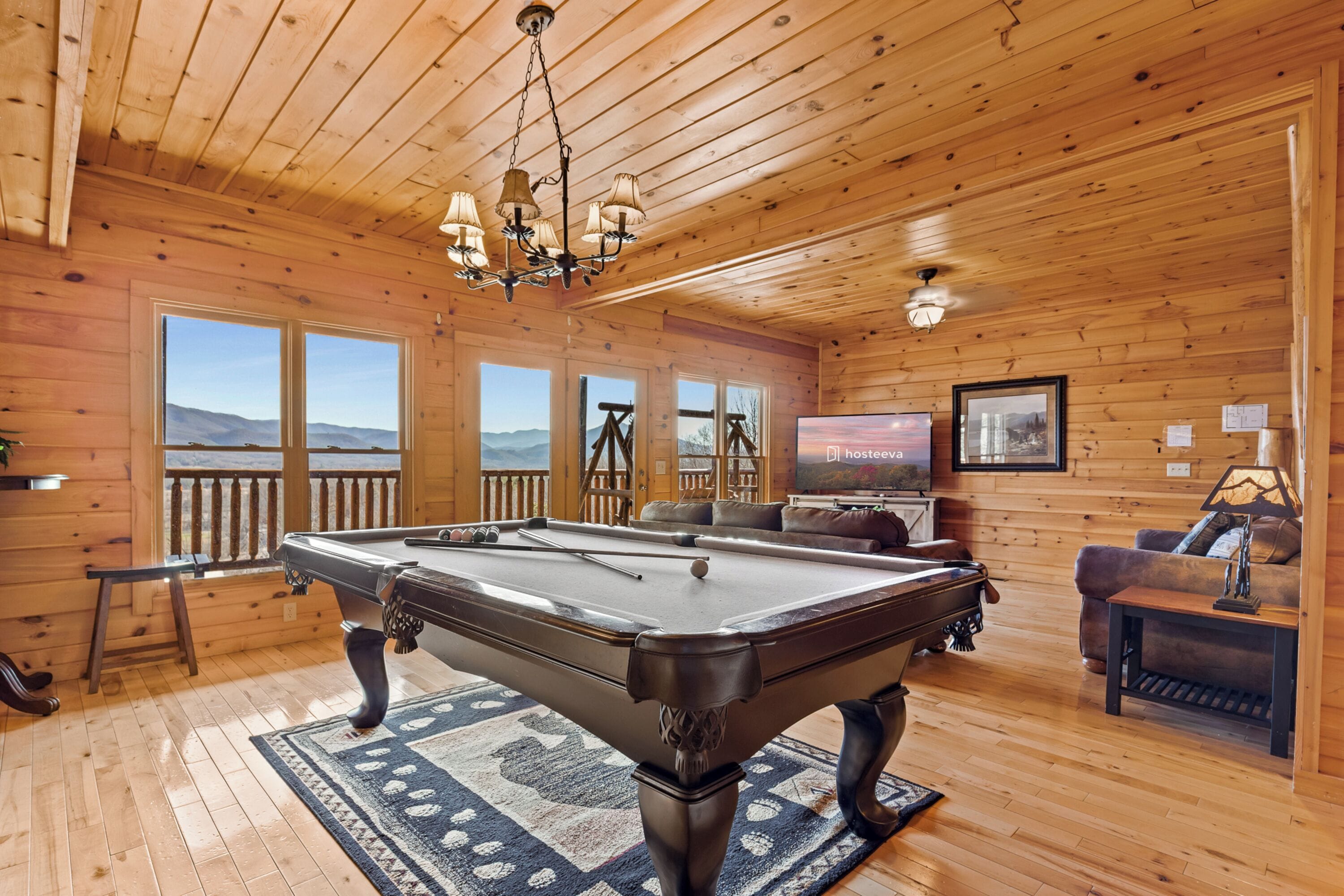 Interior de una cabaña de madera con mesa de billar, sofá y televisor.