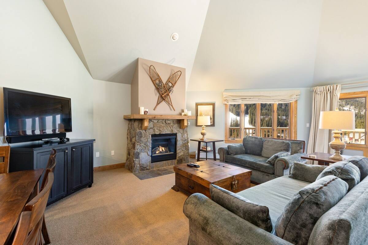 A living room with a stone fireplace, a television, a sofa, and a dining area.