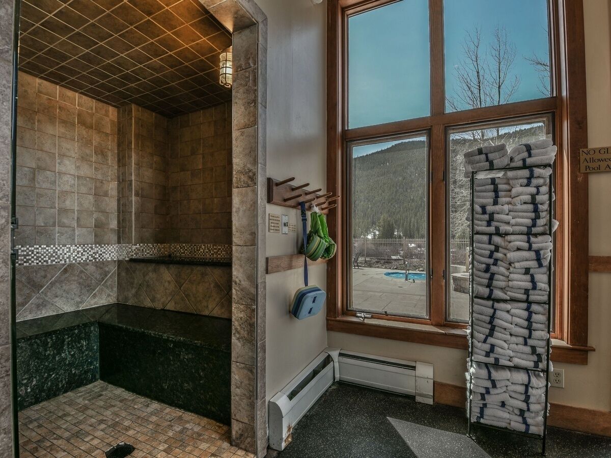 A sauna room with a tiled floor, a bench, and a window with a view of trees and a pool.