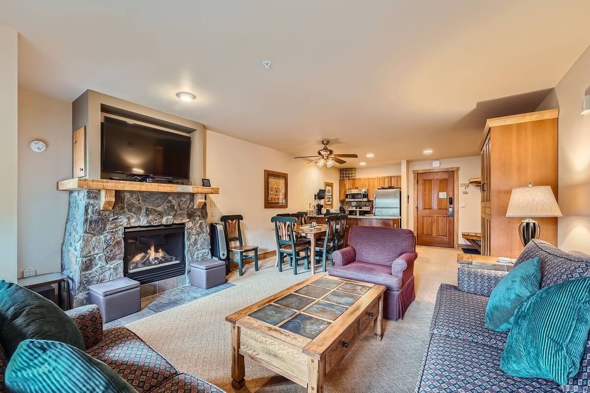 A living room with a stone fireplace, a television, and a dining area with wooden furniture.