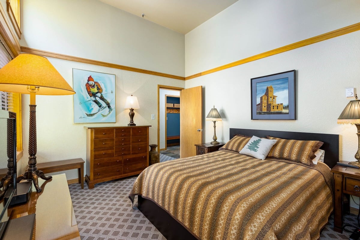 A hotel room with a large bed, wooden dresser, two lamps, and two framed pictures on the walls.