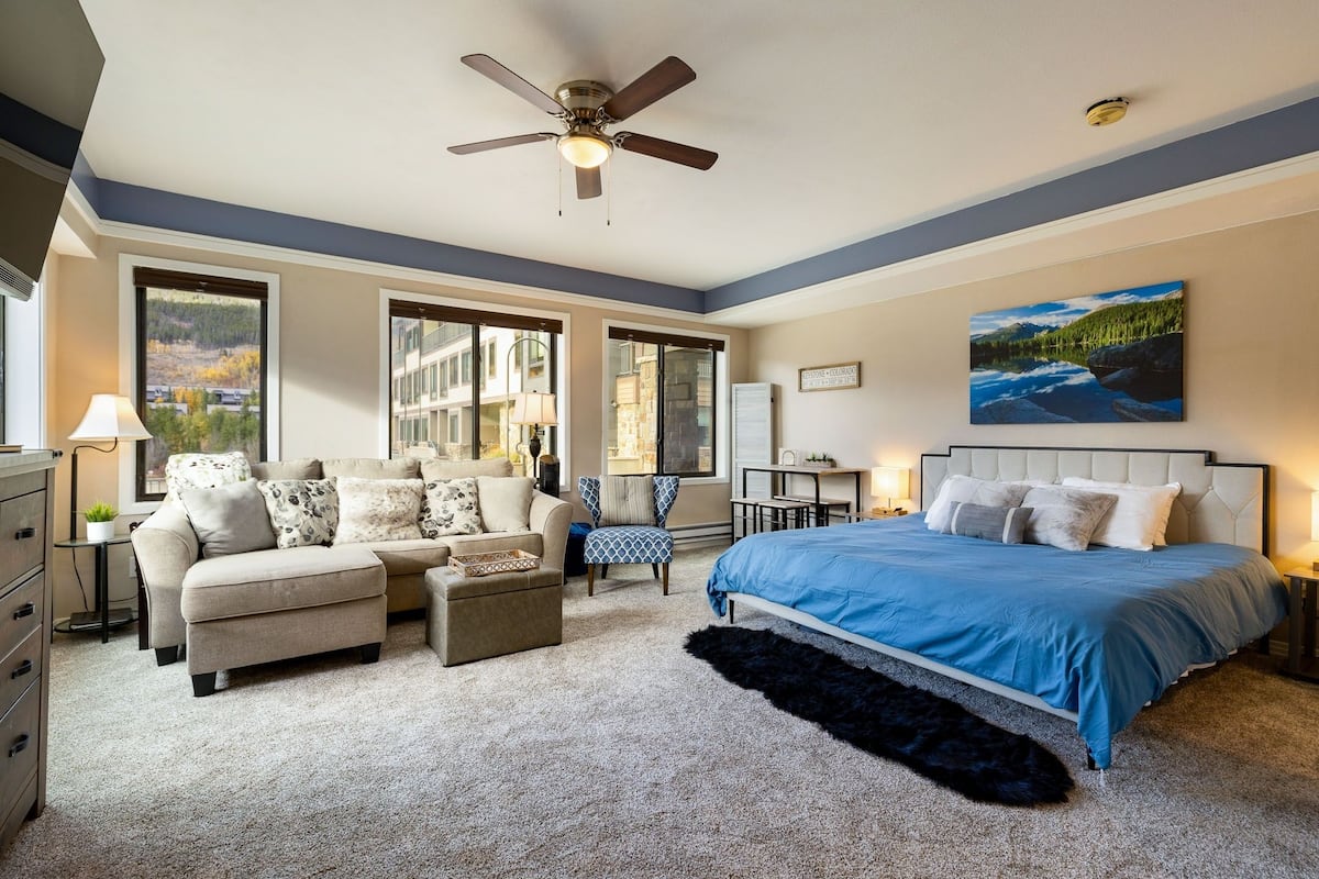A bedroom with a bed, a sofa, a chair, a desk, and a large window.