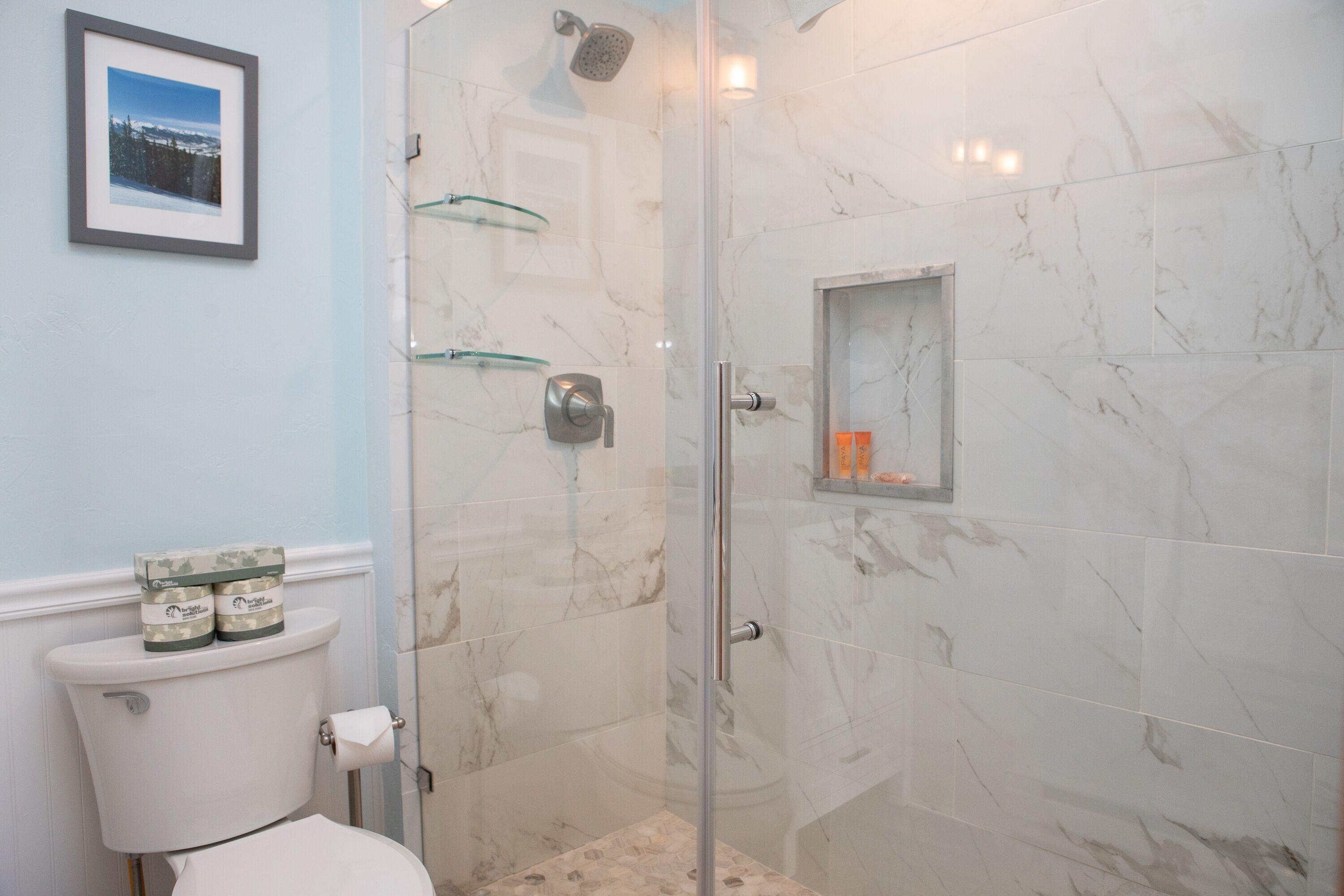 A bathroom with a toilet, a glass shower enclosure, and a marble-tiled wall.
