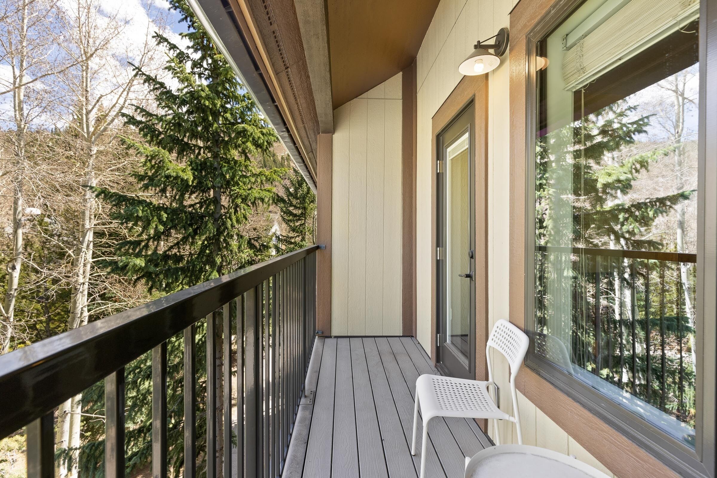 Un balcone con pavimento in legno, una sedia bianca e una porta in vetro.