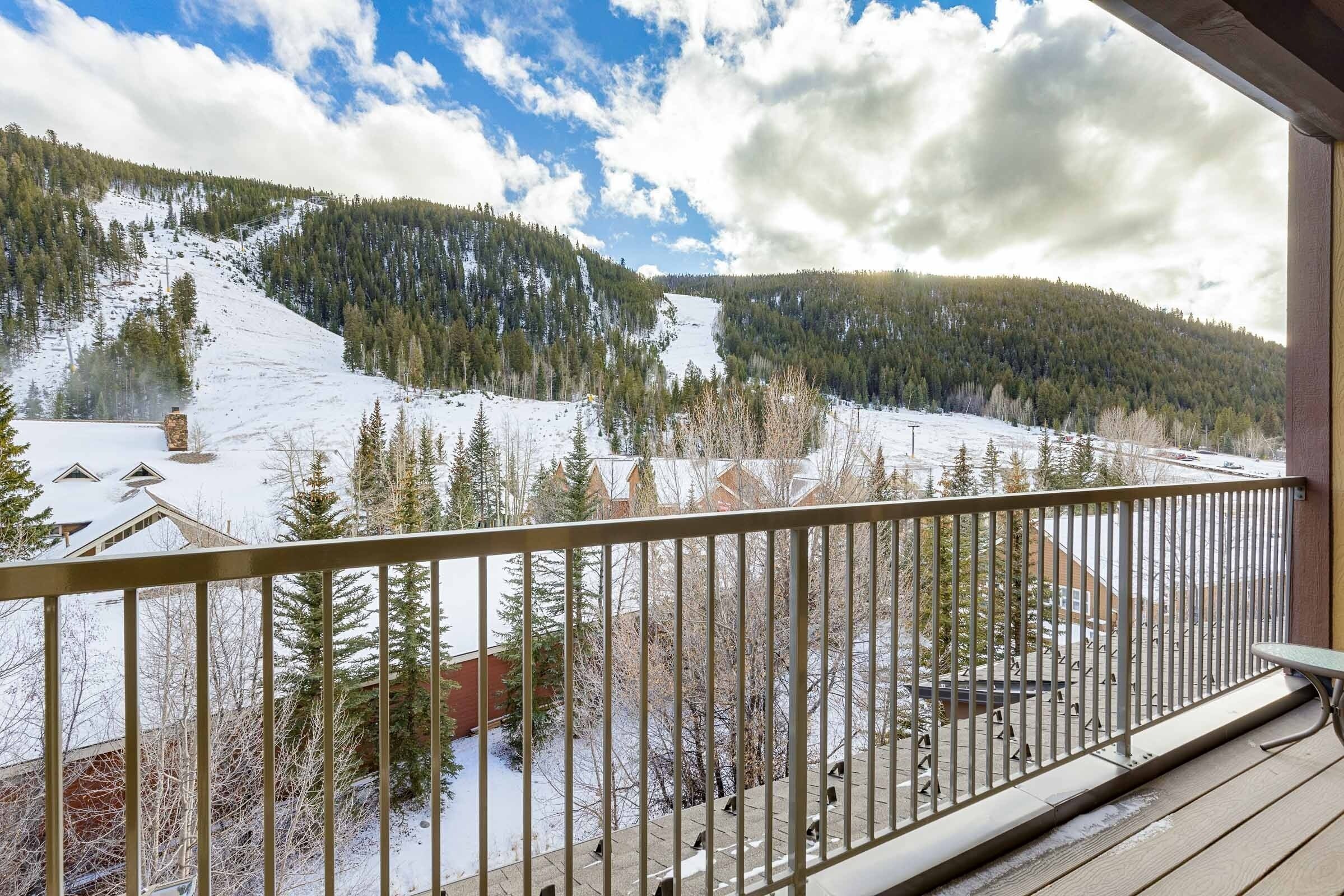 A balcony with a view of a snowy mountain landscape, a wooden deck, and a metal railing.