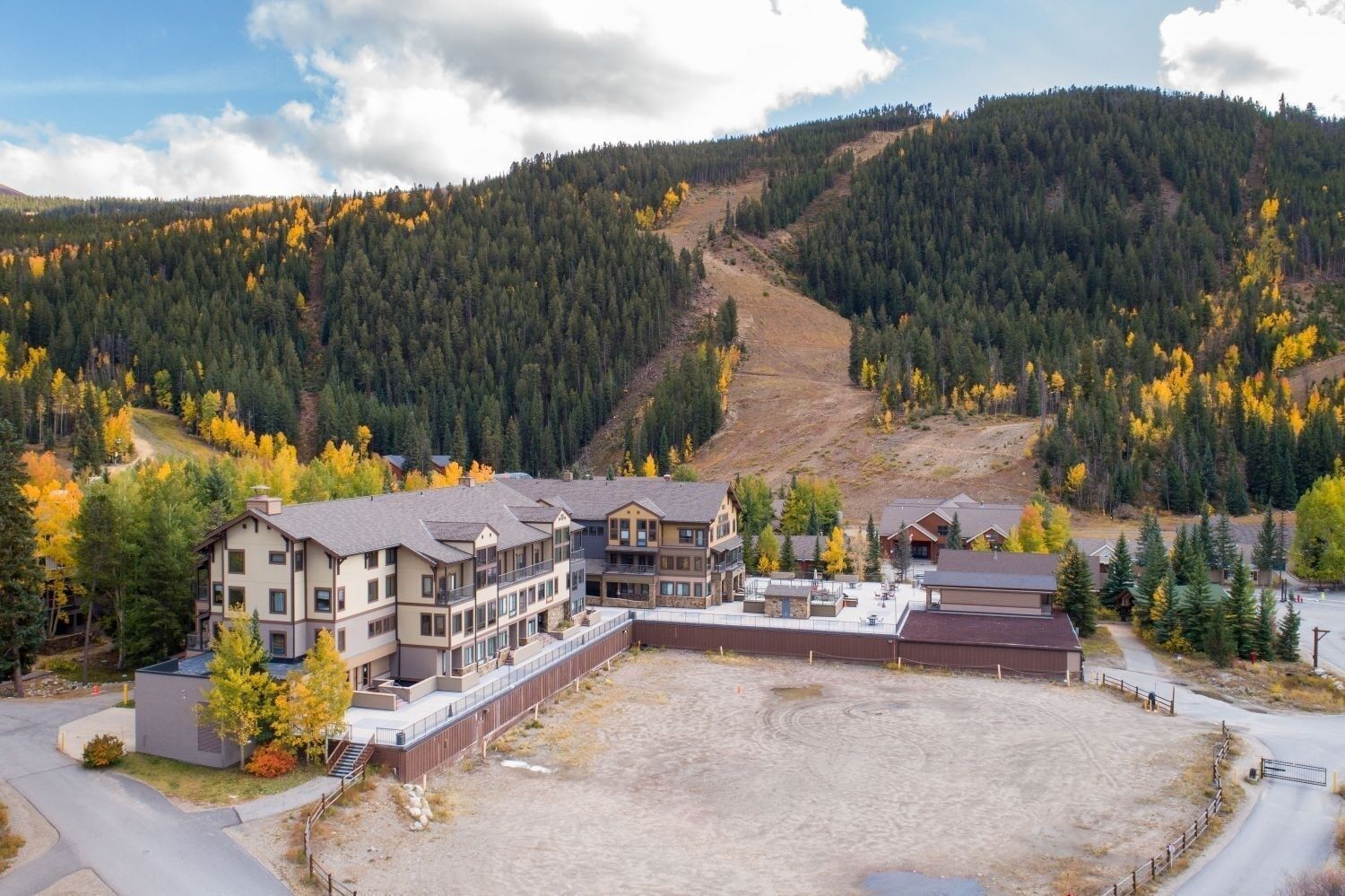 A multi-story lodge with a central courtyard, surrounded by forested hills and autumn foliage.