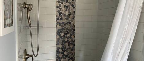 A shower with a handheld showerhead, a glass door, and a pebble-patterned wall.