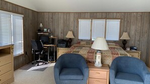 Une chambre à coucher avec un lit, deux chaises, un bureau, un ordinateur et une lampe.