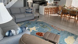 Un salon comprenant un canapé, une table basse, un tapis à motifs, un escalier, un coin cuisine et un ensemble de salle à manger.