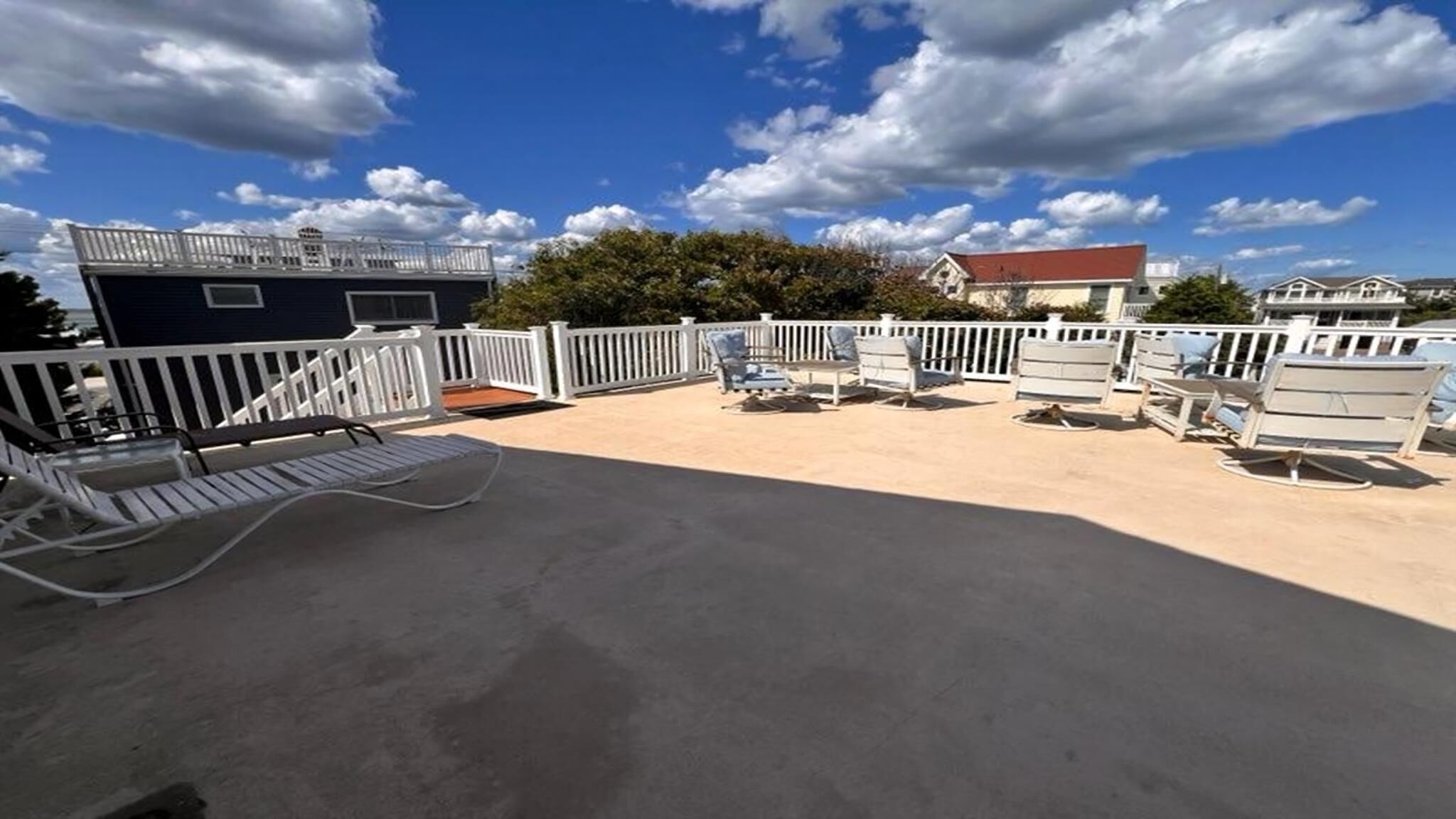 A rooftop patio with white railings, lounge chairs, and a view of the ocean.