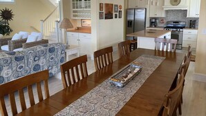 Une cuisine moderne avec des meubles blancs, un réfrigérateur en acier inoxydable et un coin repas comprenant une table et des chaises en bois.