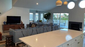Una cocina moderna con una isla central, un comedor con sofá y un televisor sobre un mueble de madera.
