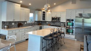 Una cocina moderna con armarios blancos, una isla central, taburetes de bar, electrodomésticos de acero inoxidable y un salpicadero con diseño.