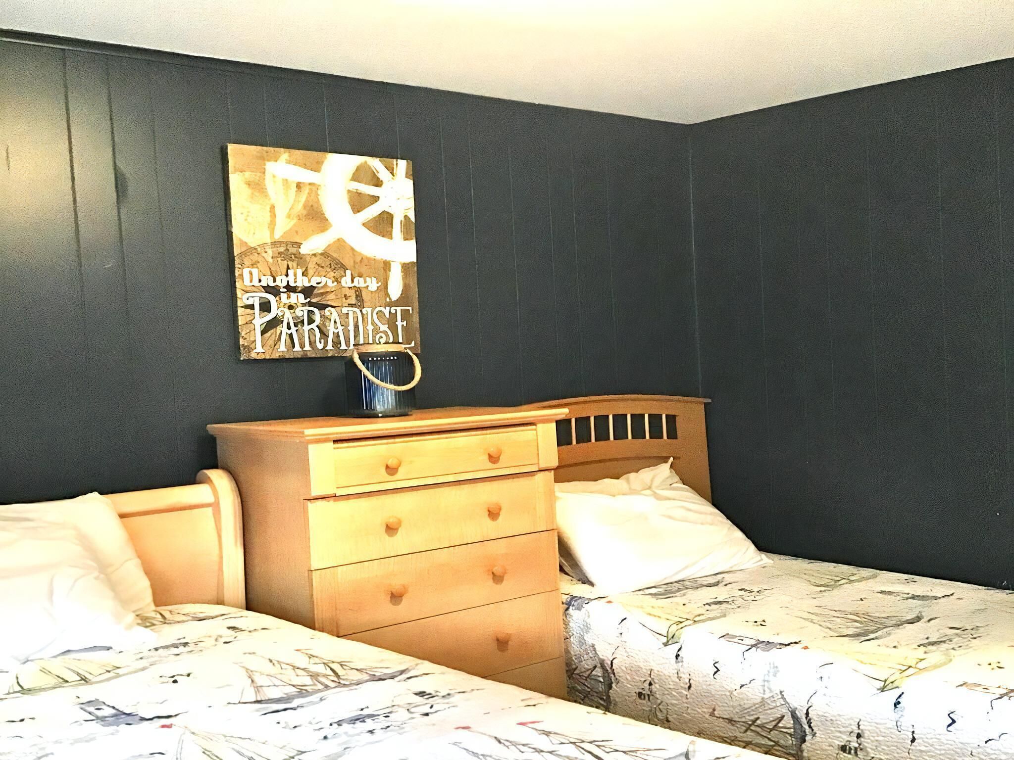 A bedroom with two beds, a wooden dresser, and a wall-mounted sign.