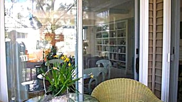 A room with a glass door, a wicker chair, a glass table with a potted plant, and a bookshelf in the background. - 4 bedroom accommodation in Harvey Cedars (Harvey Cedars)
