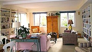 A spacious living room with a large window, a wooden cabinet, a dining table with chairs, and a bookshelf. - 4 bedroom accommodation in Harvey Cedars (Harvey Cedars)