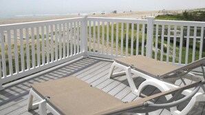 Una terraza con dos sillones de descanso y una valla blanca con vista a una playa.