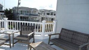 A balcony with a white railing, wicker furniture, and a view of coastal buildings. - 4 bedroom accommodation in Harvey Cedars (Harvey Cedars)