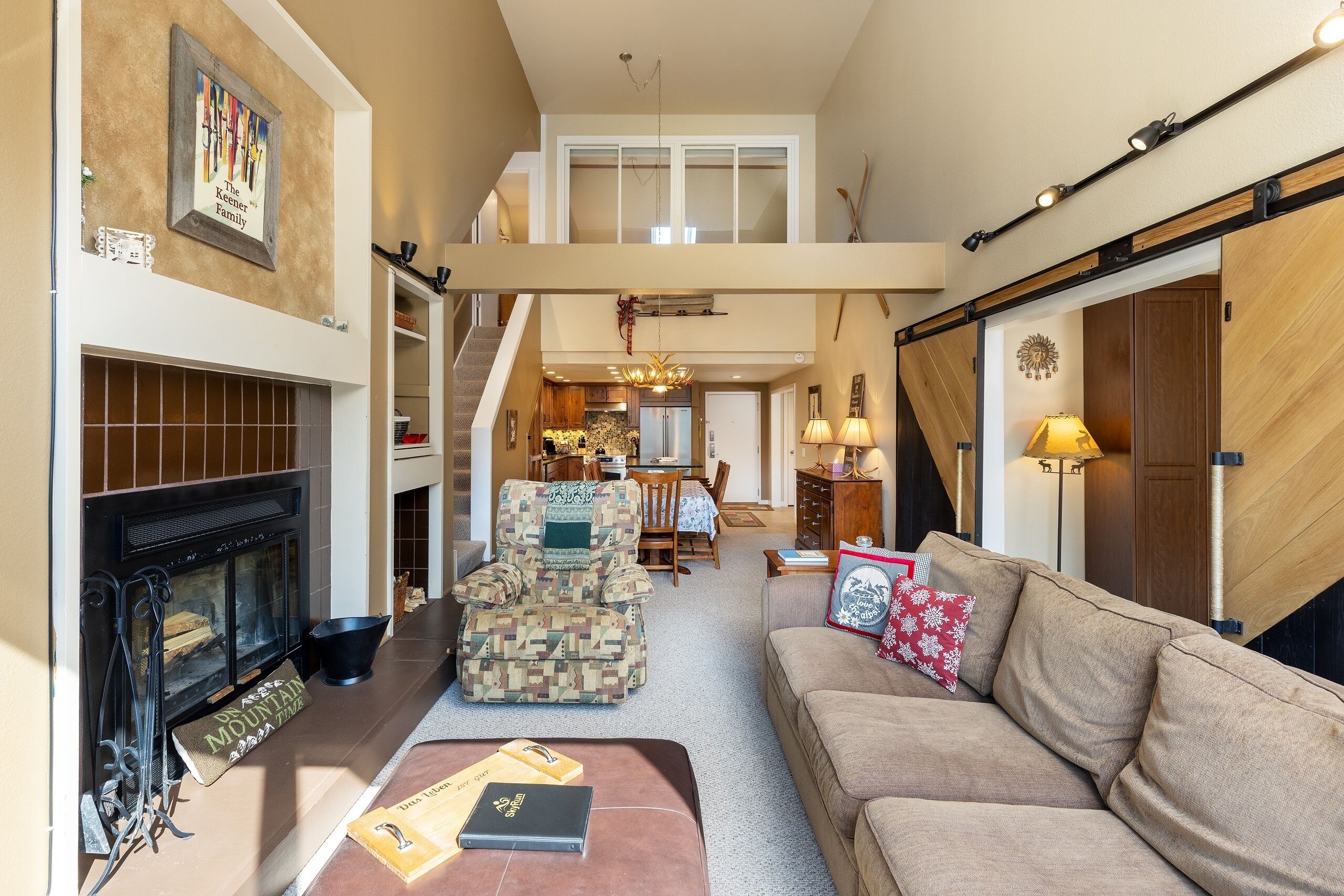 A spacious living room with a fireplace, a patterned armchair, a sofa, and a dining area in the background.