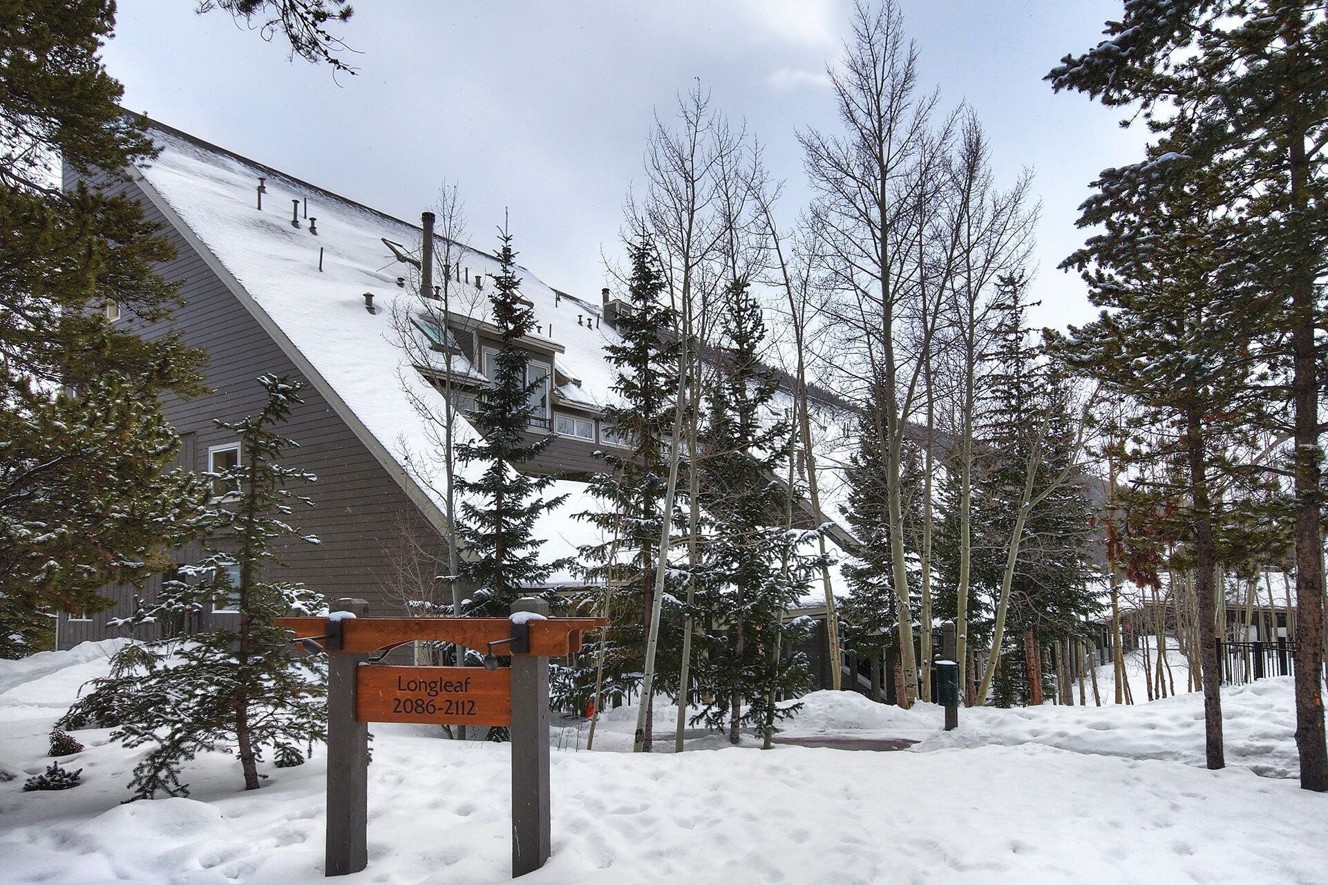 A snow-covered residential area with a house, a sign reading "Longleaf 2086-2112," and leafless trees.
