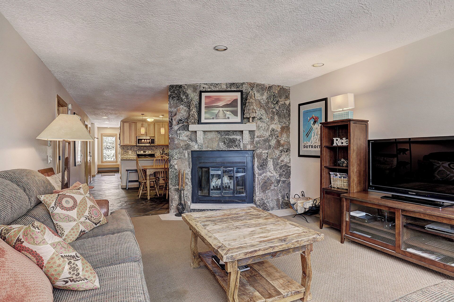 A living room with a stone fireplace, a television, and a dining area with wooden furniture.