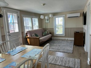 A cozy living room with a sofa, a dining table with chairs, and a wooden cabinet.
